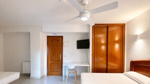 Habitación de hotel con cama, escritorio, silla, armario, ventilador de techo y televisor.
