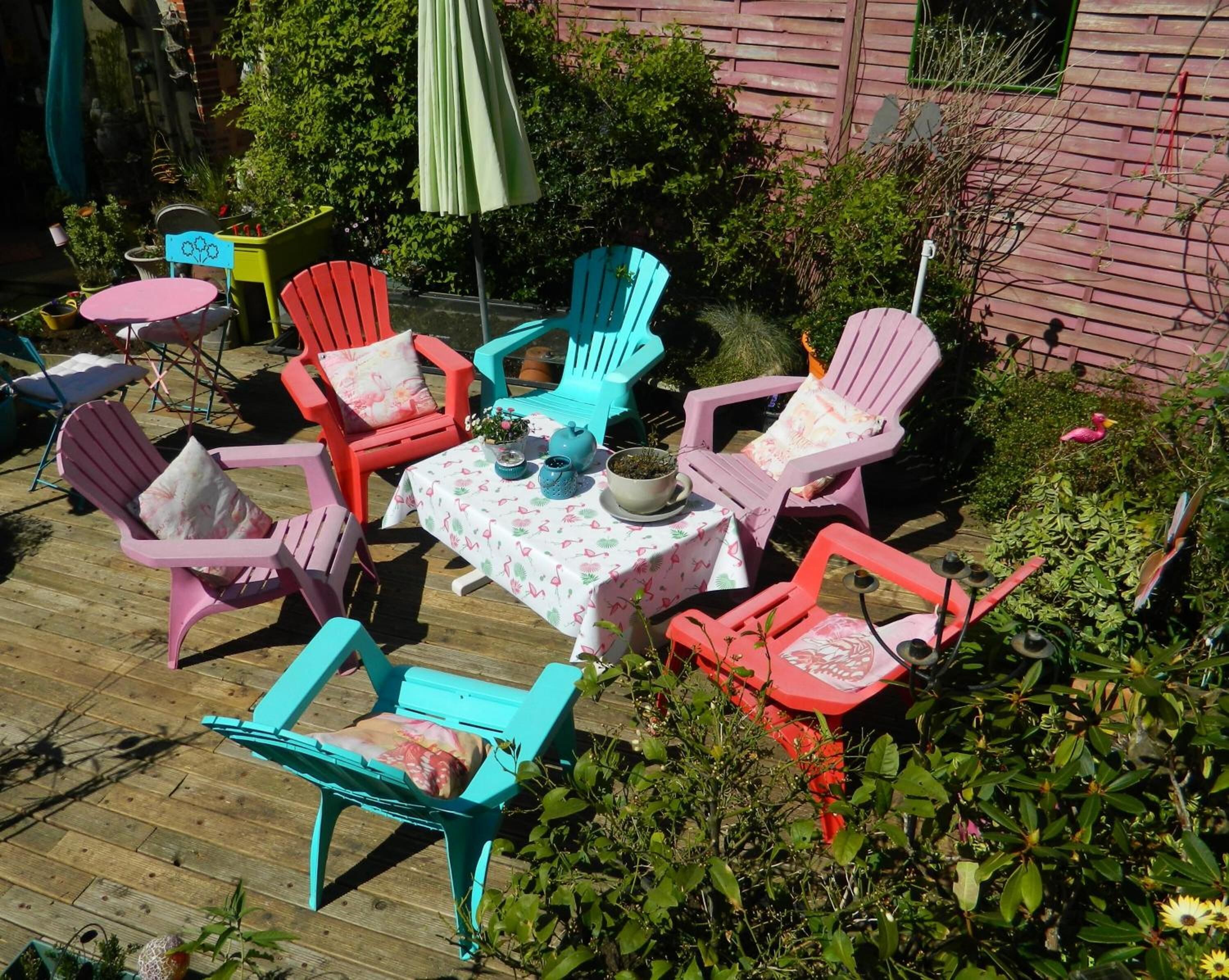 Un patio al aire libre con sillas Adirondack de colores, una mesa con mantel floreado y plantas en macetas.