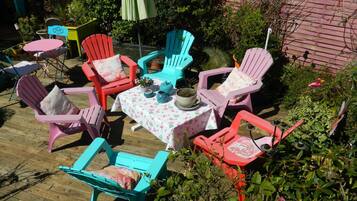 Un patio al aire libre con sillas Adirondack de colores, una mesa con mantel floreado y plantas en macetas.