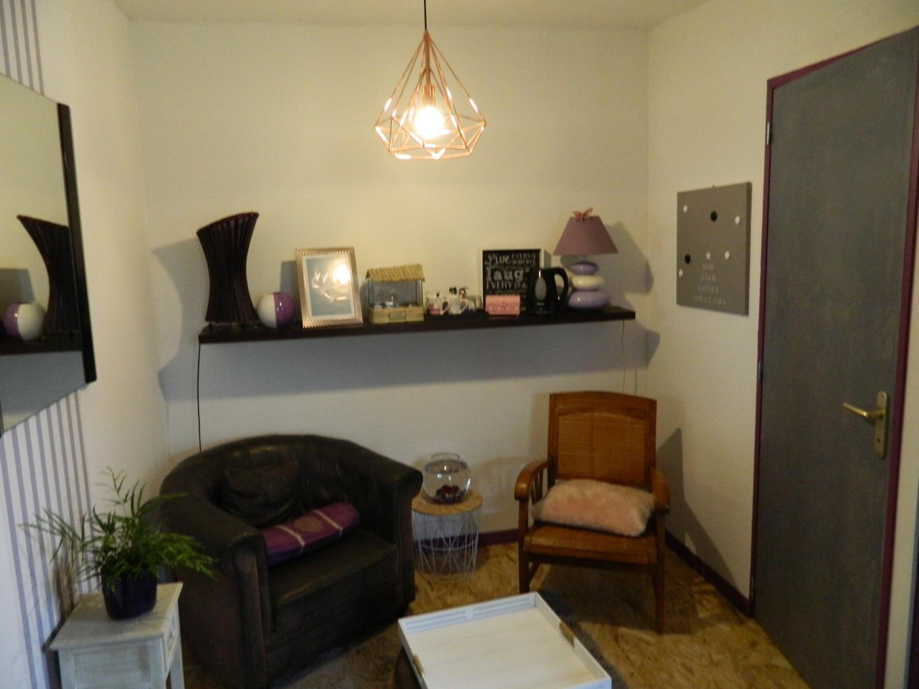 Una sala de estar acogedora con un sofá de cuero oscuro, un sillón de madera, una mesita redonda y una estantería con diversos objetos decorativos.