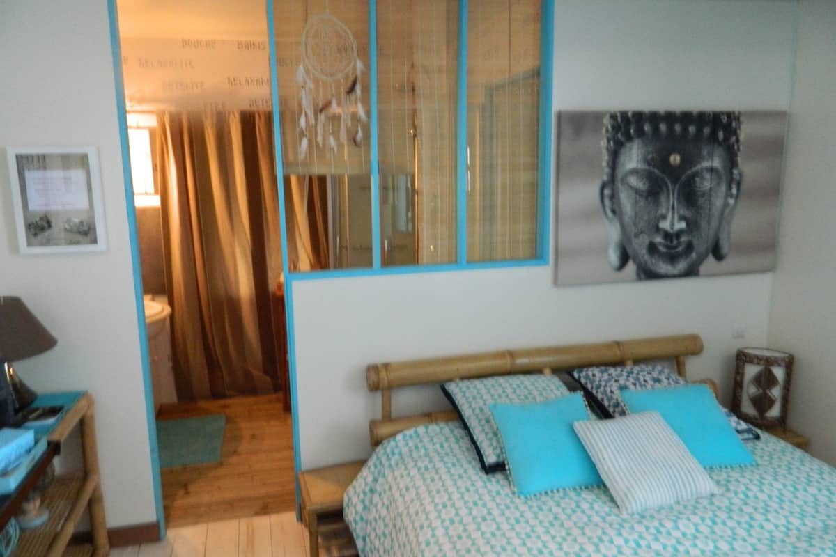 A bedroom with a bed, a nightstand, a wall-mounted shelf, a window with curtains, and a door leading to another room.