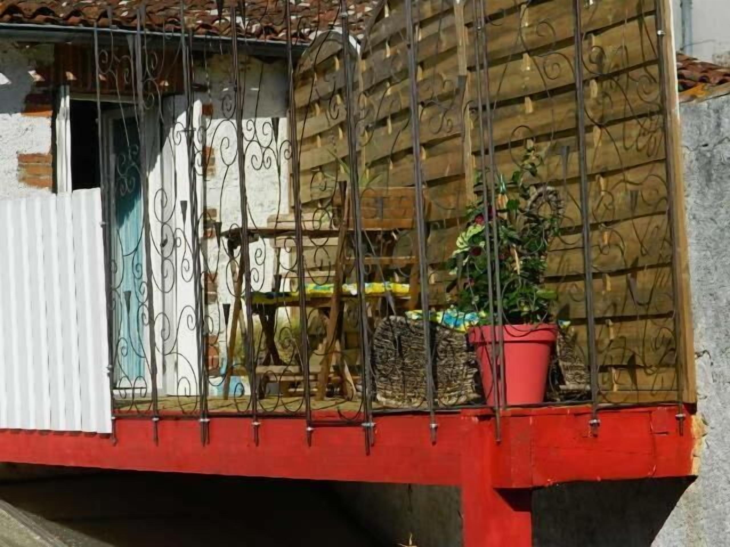 A balcony with a red railing, a potted plant, and a metal gate.