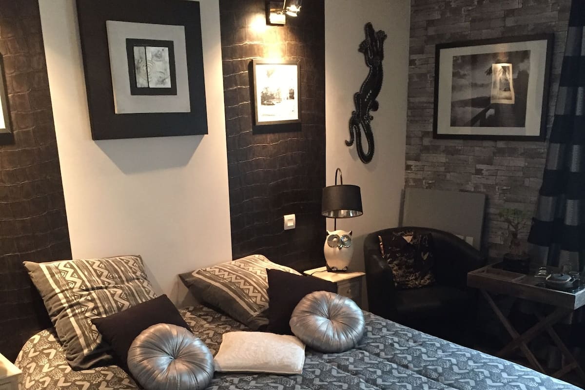 A bedroom with a patterned bedspread, multiple pillows, a side table with a lamp, and framed pictures on the walls.