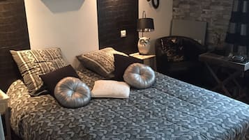 Une chambre à coucher avec une couvre-lit à motifs, plusieurs coussins, une table de chevet avec une lampe et des tableaux encadrés accrochés aux murs.