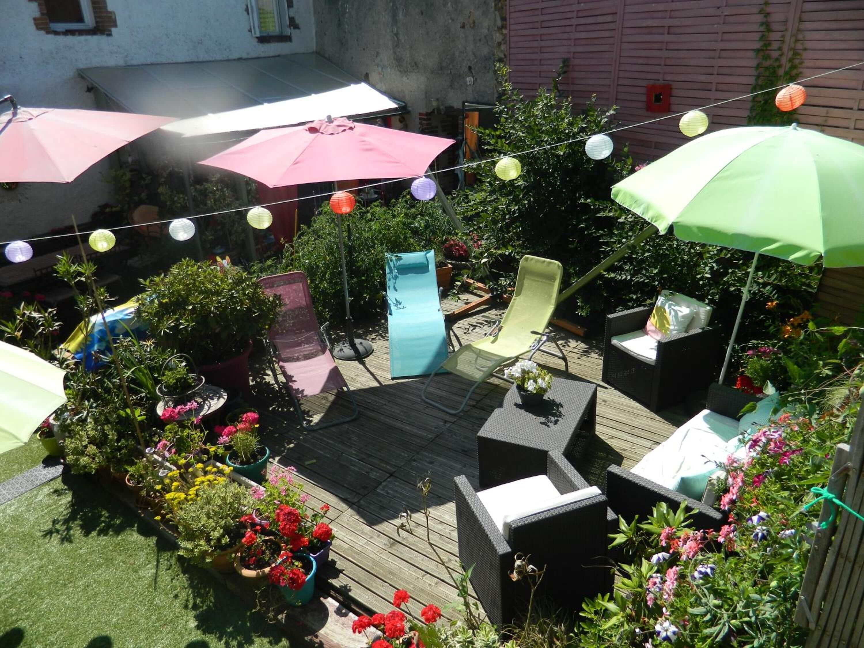 Una terraza de madera con mobiliario exterior, plantas en macetas y luces colgantes.