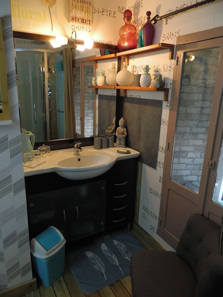 Un baño pequeño con un lavamanos blanco, muebles oscuros, un cubo de basura azul y una alfombra pequeña.
