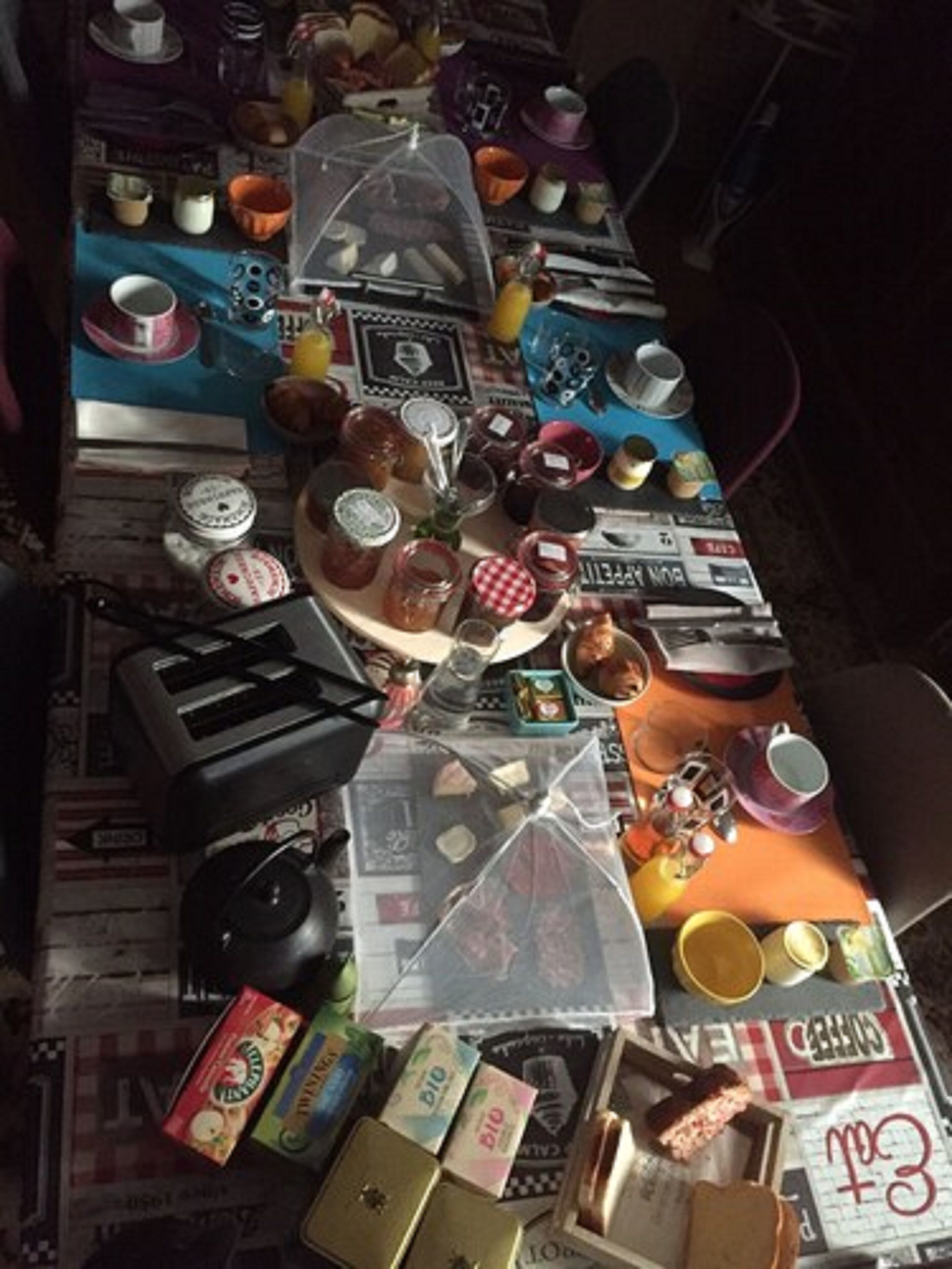 A table set with various food items, including jars, cups, and plates, on a table covered with newspapers.
