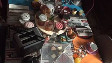 A table set with various food items, including jars, cups, and plates, on a table covered with newspapers.