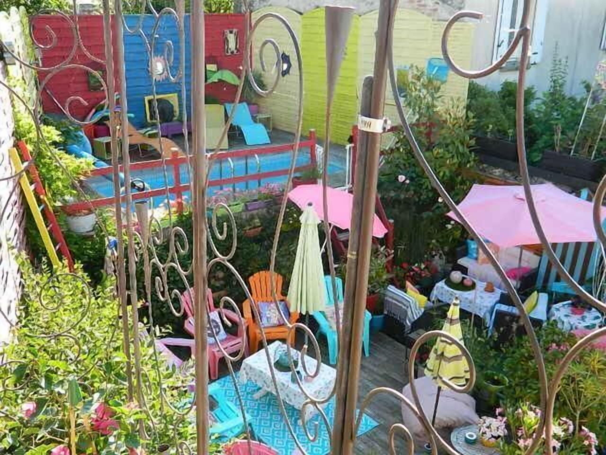 A colorful outdoor area with various seating arrangements, including chairs and tables, surrounded by plants and decorative elements.