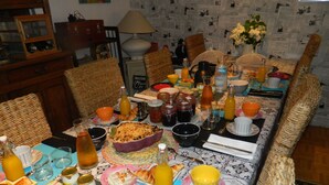 A dining table set with various dishes, drinks, and utensils, surrounded by wicker chairs.
