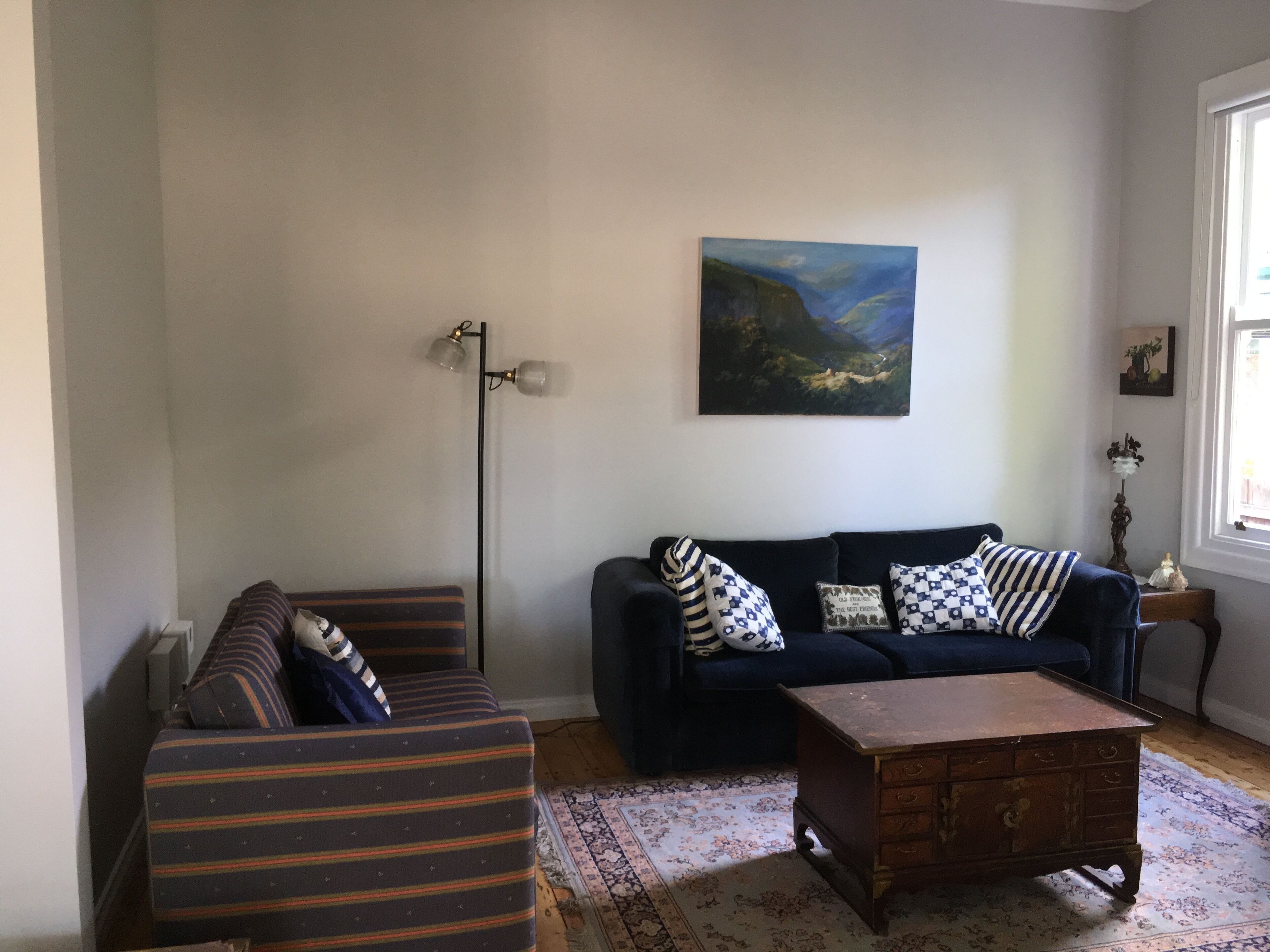 Een zithoek met een donkerblauwe bank, gestreepe fauteuils, een houten salontafel en een schilderij aan de muur.