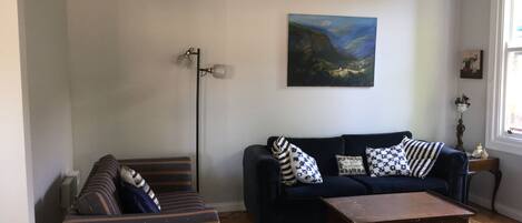 Een zithoek met een donkerblauwe bank, gestreepe fauteuils, een houten salontafel en een schilderij aan de muur.