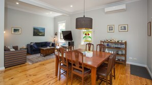 A dining area with a wooden table and chairs, a television, and a decorative shelf with glassware. - Central, Classic, Contemporary , Comfortable, Convenient , Charming (Ballarat Central)