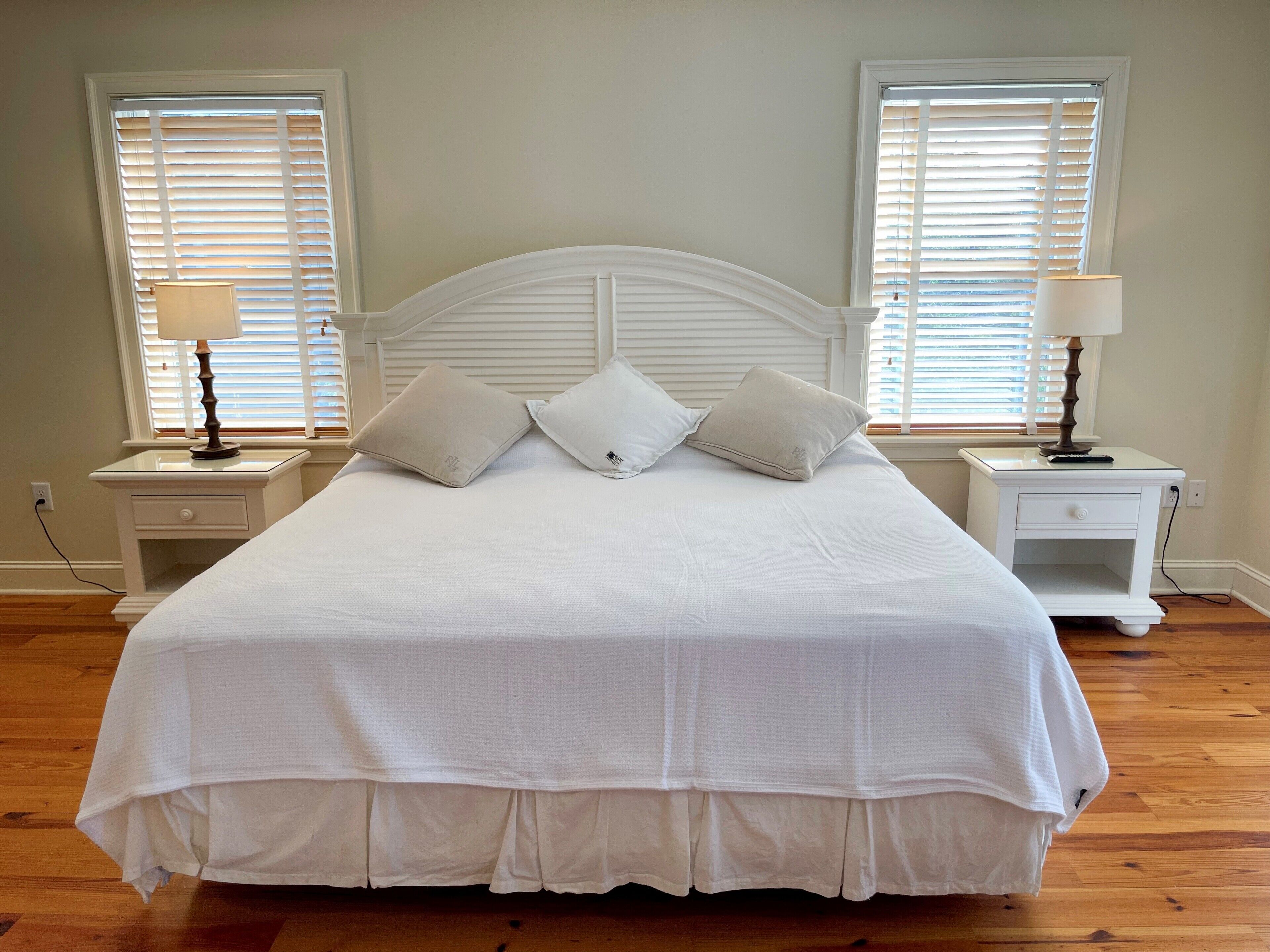 A neatly made bed with a white headboard, two bedside tables with lamps, and a window with blinds.