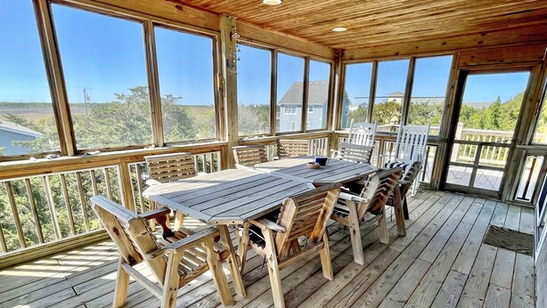 Une terrasse en bois avec une table et des chaises, de grandes fenêtres et une vue sur le paysage environnant.