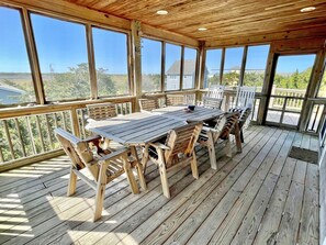 A wooden deck with a table and chairs, large windows, and a view of the surrounding landscape. - Last Clear Chance: Spectacular spacious home, pool table (Ocracoke)
