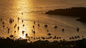 A coastal scene with boats on calm waters, a distant shoreline with buildings, and palm trees. - La Bella Vita: Full AC! Pool! Sunset Views All Year! (St. John)