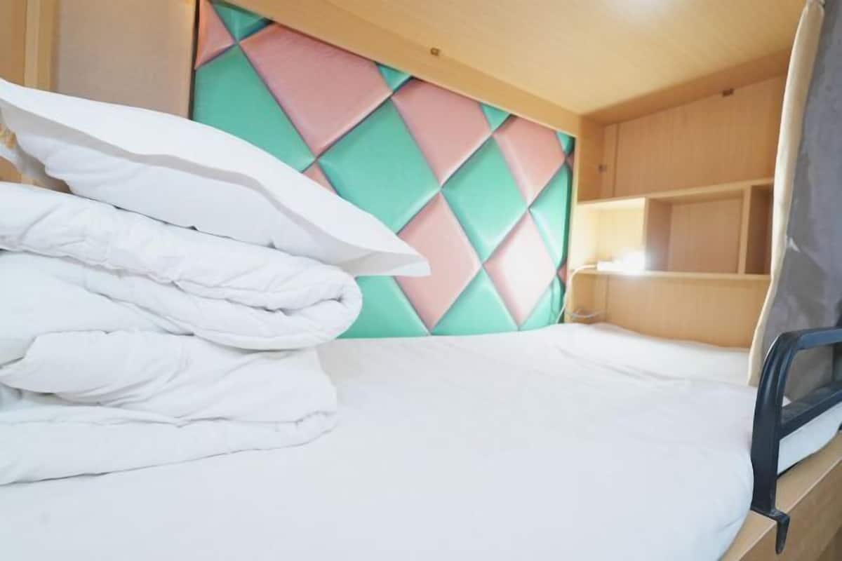 Un lit superposé avec une tête de lit colorée, un lit bien fait avec une literie blanche et une armoire en bois sur la droite.