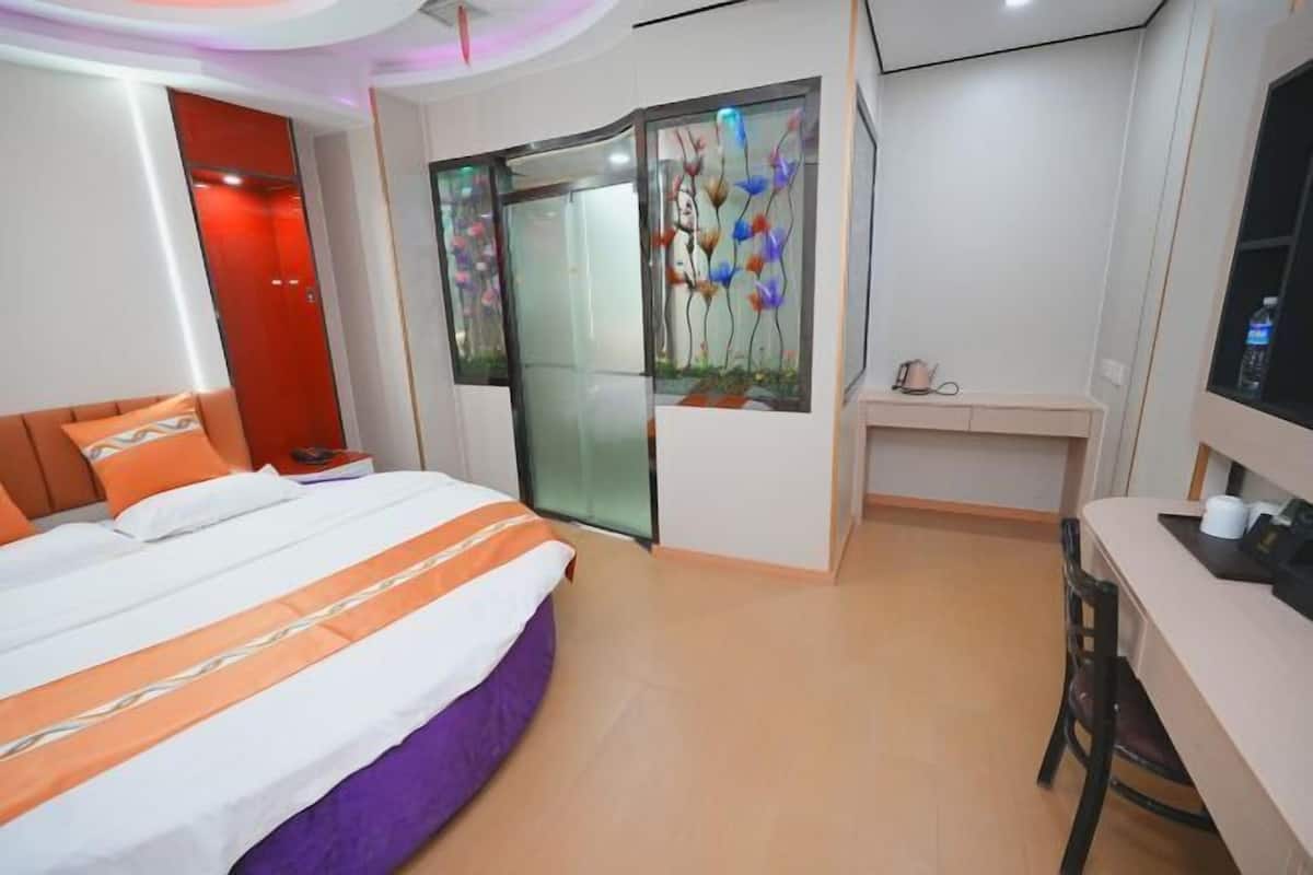 Une chambre d’hôtel équipée d’un lit, d’un bureau, d’une chaise, d’une télévision et d’une cloison en verre décorée d’œuvres d’art.