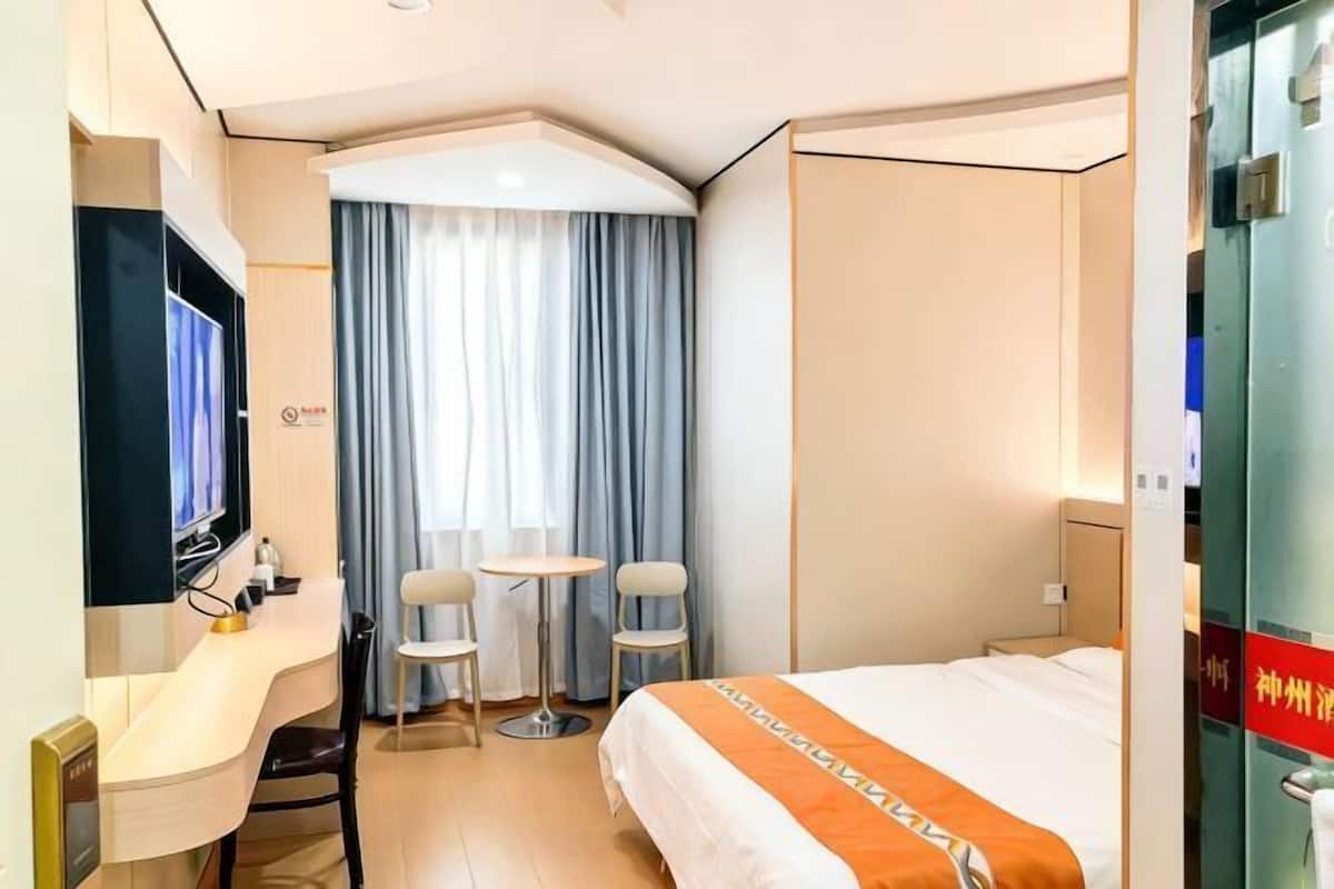 Une chambre d’hôtel avec un lit, un bureau, deux chaises, une télévision et une fenêtre avec des rideaux.