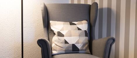 A corner room with a grey armchair, a floor lamp, and a striped wall.