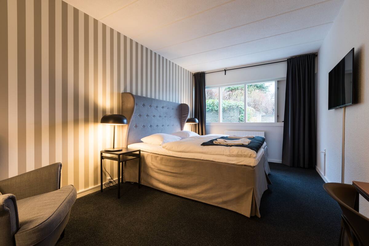 A hotel room with a bed, a chair, a TV, and a window with curtains.