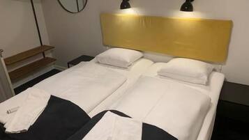Una cama doble con cabecera, dos mesitas de noche y un espejo en la pared.