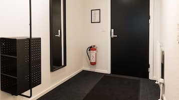 Un pasillo con un felpudo negro, una puerta negra, un extintor y un estante negro sujeto a la pared.