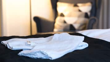 A neatly made bed with a white towel and a bottle on the bed.