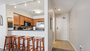Una cocina con armarios de madera, un microondas y un refrigerador. Hay tres taburetes de madera y una encimera.