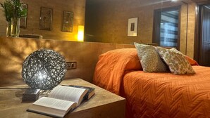 Une chambre à coucher avec un grand lit, une table de chevet sur laquelle repose un livre, une lampe décorative et des œuvres d’art encadrées accrochées au mur.