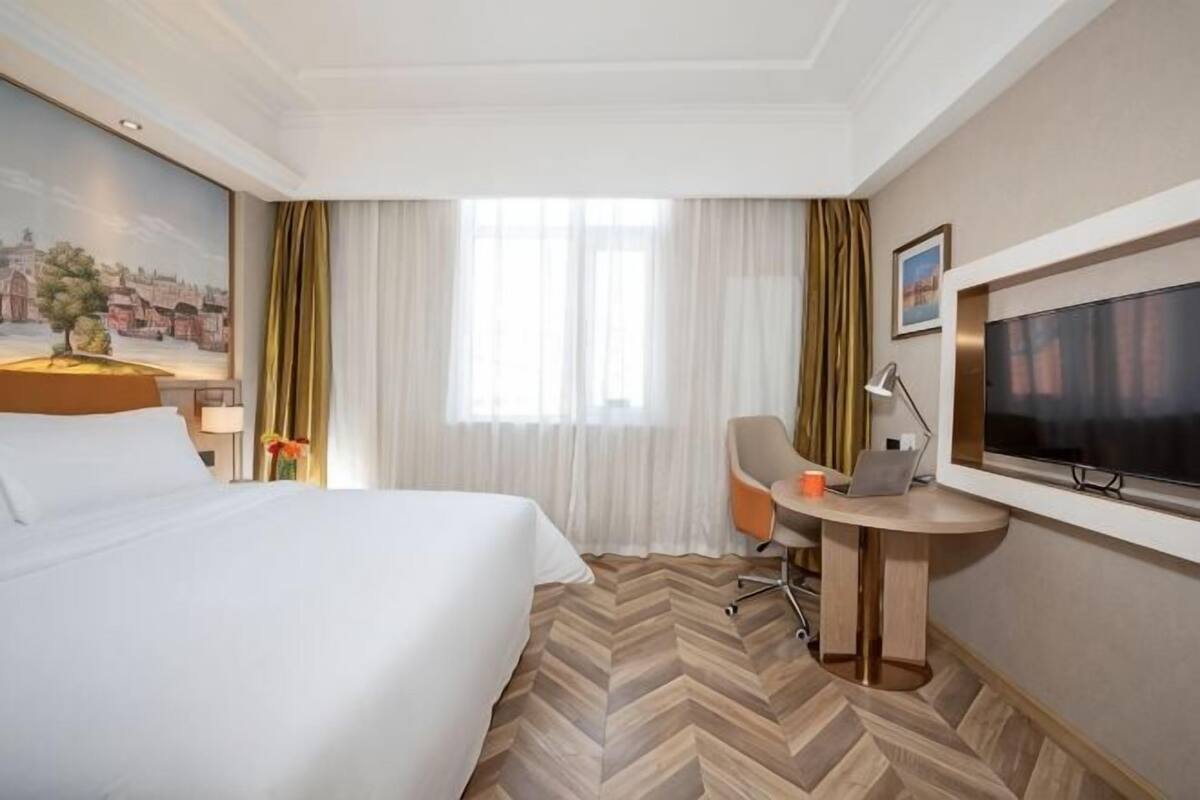 Ein Hotelzimmer mit Bett, Schreibtisch mit Stuhl, Fernseher und einem Fenster mit Vorhängen.
