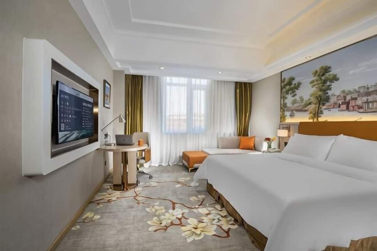 A hotel room with a bed, desk, TV, and a painting on the wall.
