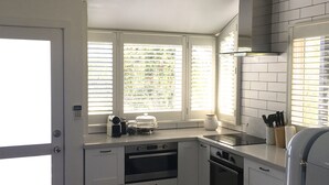 Een moderne keuken met witte kasten, een ingebouwde oven, een kookplaat en een raam met jaloezieën.