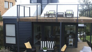 Een modern huis met een houten terras, buitenmeubels en een glazen deur naar binnen.