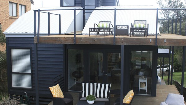 A modern house with a wooden deck, outdoor seating, and a glass door leading to the interior.