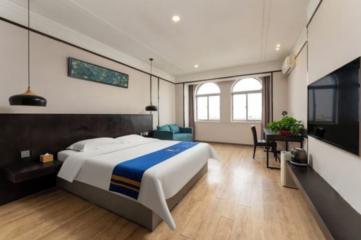 A modern hotel room with a large bed, a desk with a chair, a television, and a window with a view.
