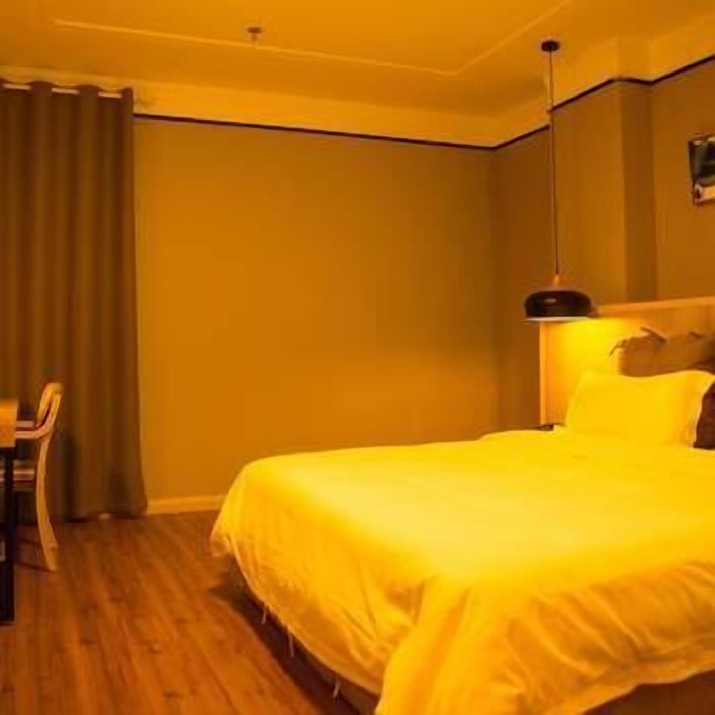 A hotel room with a large bed, a desk with a chair, and a single wall-mounted lamp.