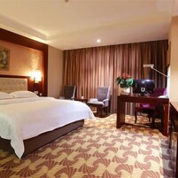 A hotel room with a large bed, a desk with a computer, a chair, and a plant.