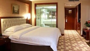 Ein Hotelzimmer mit einem großen Bett, einem Nachttisch, einer Lampe, einem Bild an der Wand und einem gemusterten Teppich.