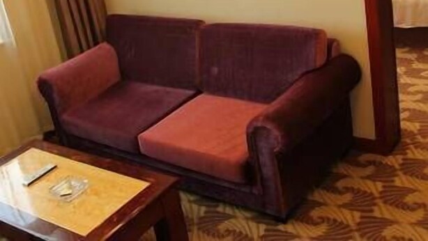A hotel room with a red sofa, a wooden side table, and a patterned carpet. - Bo Jue Holiday Inn (Hefei)