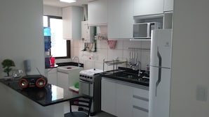 A modern kitchen with white cabinets, a black countertop, a gas stove, a microwave, and a sink. - Para 9 Pessoas ao Lado Shopping Rio Mar (Fortaleza)