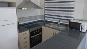 Una cocina con un refrigerador blanco, estufa, microondas y ventana a rayas.