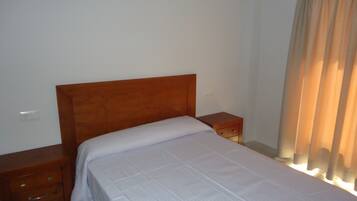 Un dormitorio con cabecera de madera, una cama individual, una mesita de noche con cajones y una ventana con cortinas.