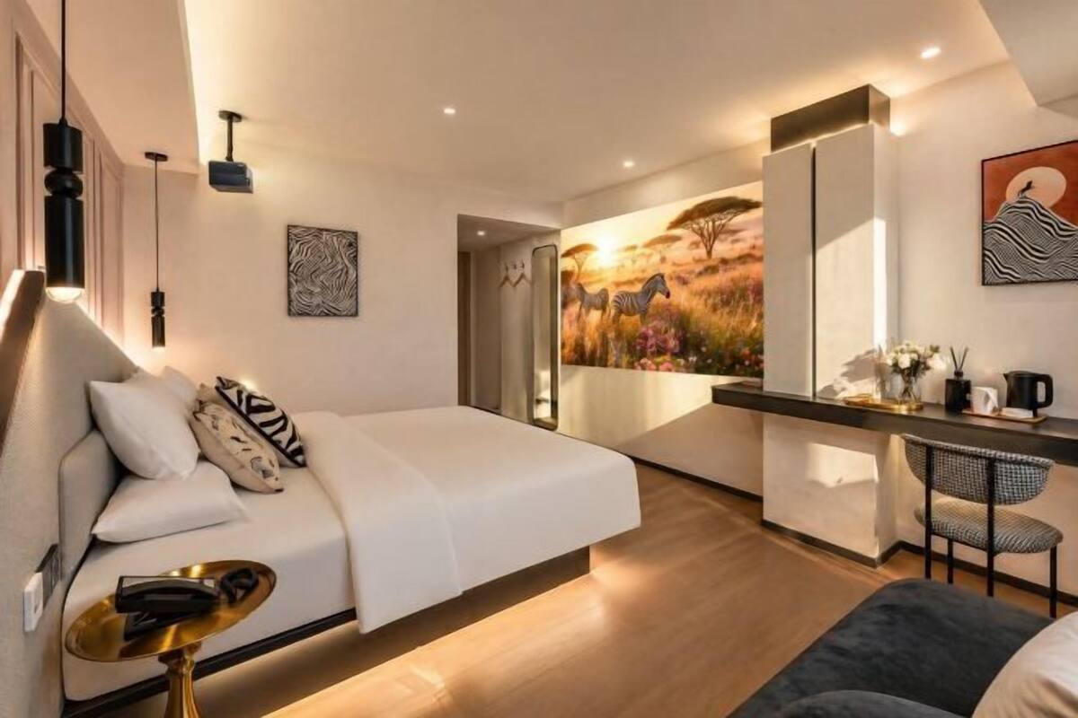 Une chambre d’hôtel moderne, équipée d’un lit, d’un bureau, d’une chaise et d’un grand tableau représentant une scène de savane.