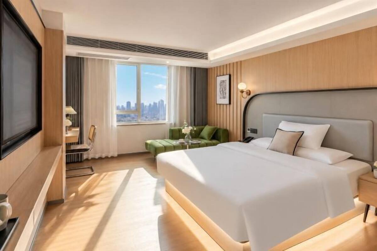 Une chambre d’hôtel moderne dotée d’un grand lit, d’un coin salon avec un canapé vert, d’une vue sur la ville et d’une télévision.