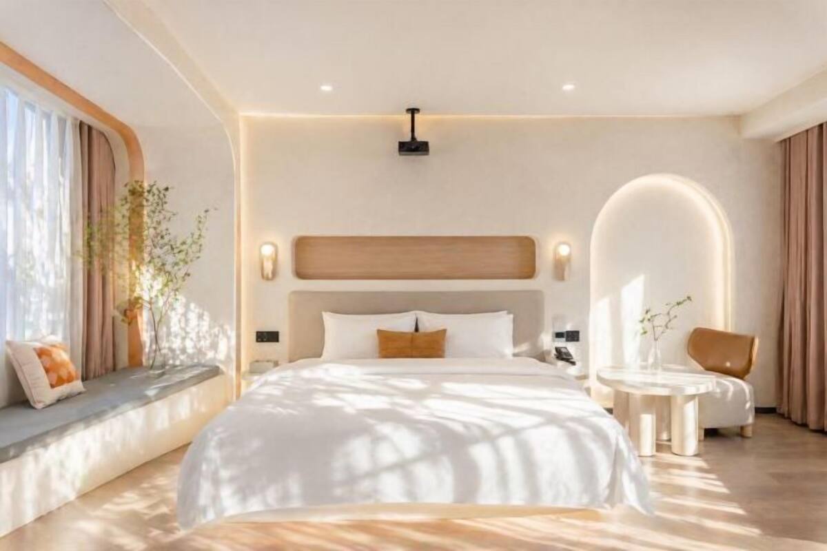 Une chambre moderne avec un grand lit, des tables de chevet, un miroir rond et une fenêtre avec des rideaux.