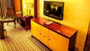 A hotel room with a wooden cabinet, a television, a chair, and a striped carpet. - Heyuan City Holiday Hotel (Heyuan)