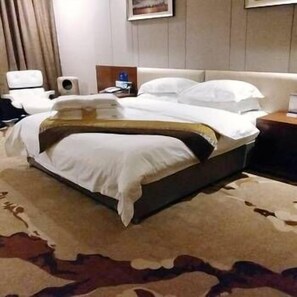 A hotel room with a large bed, a bedside table, a chair, and a wall-mounted TV.