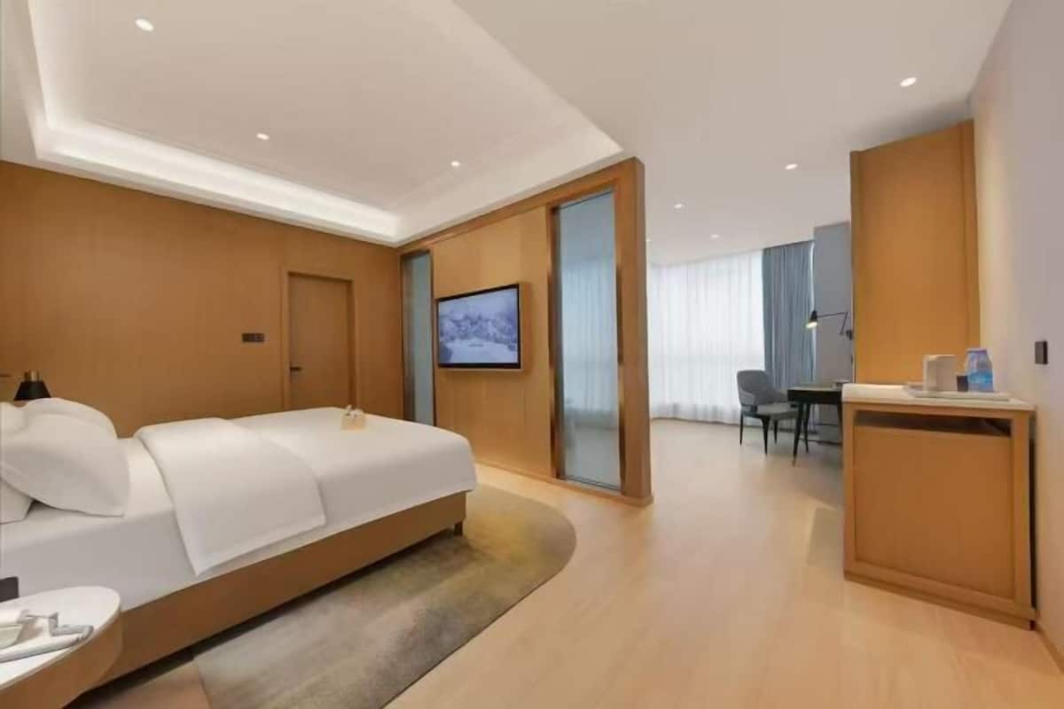 A modern hotel room with a bed, a TV, a desk, and a chair.